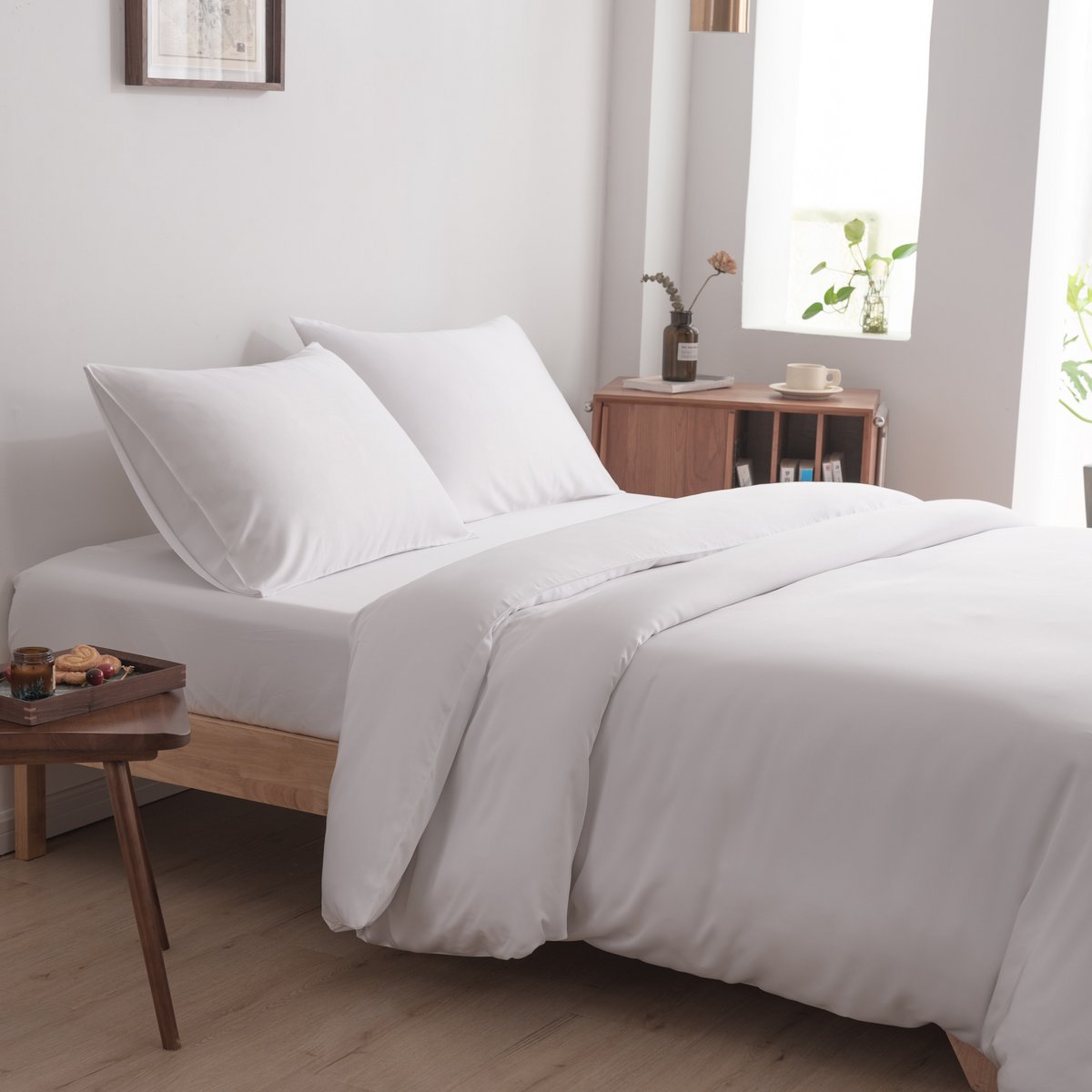 Bamboo duvet cover in Coco White on a bed with two pillows in a sunlit bedroom with a nightstand and plant