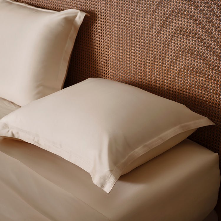 Tencel™ Sateen Pillowcase in White Sand styled on a bed against a rattan headboard
