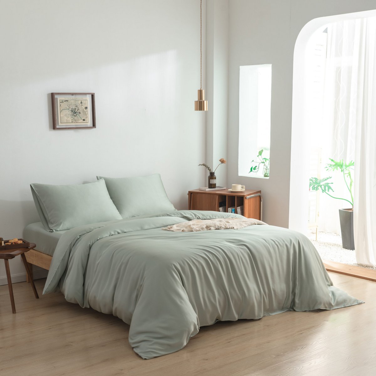 Bamboo duvet cover in Sage Green on a bed near a window with a plant in a sunlit bedroom