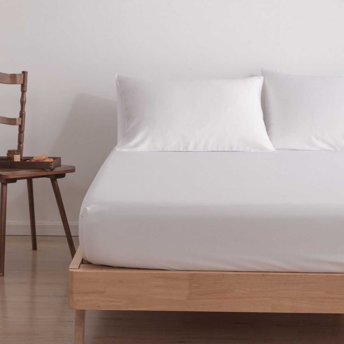 Coco White bamboo fitted sheet on a bed beside a wooden chair, close angled bedroom view.
