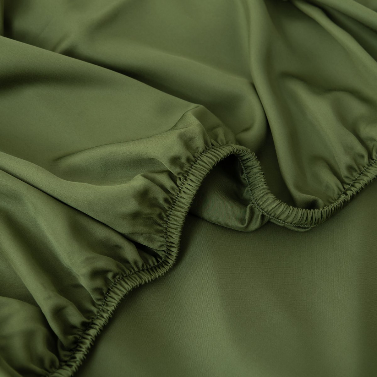 Close-up of the Deep Moss bamboo fitted sheet's folded elastic corner off the mattress.