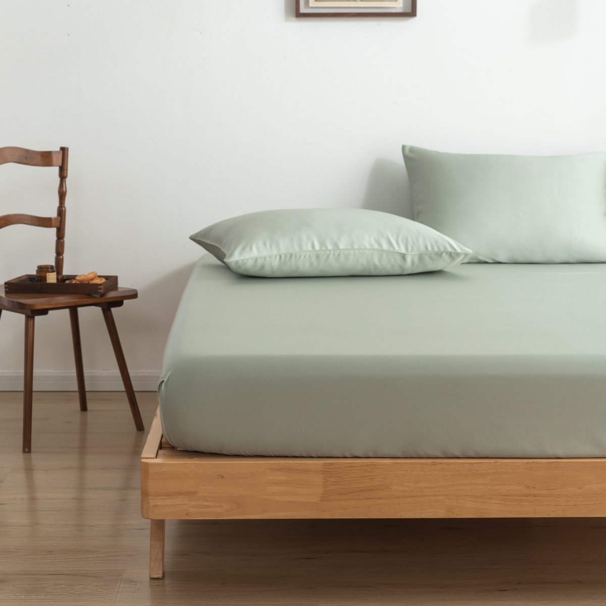 Sage Green bamboo fitted sheet on a bed beside a wooden chair with a breakfast tray.